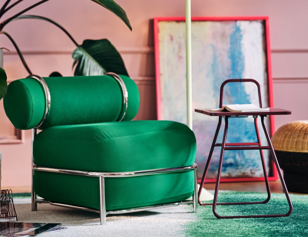 A green inflatable IKEA PS 2026 lounge chair held inside a tubular chrome frame, beside a small burgundy table.